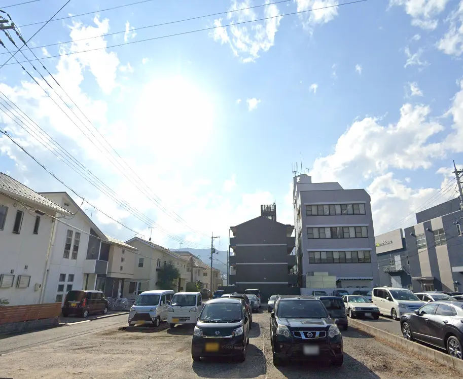 駐車場とその周辺の住宅街の風景。青空の下で静かな街並みが広がる